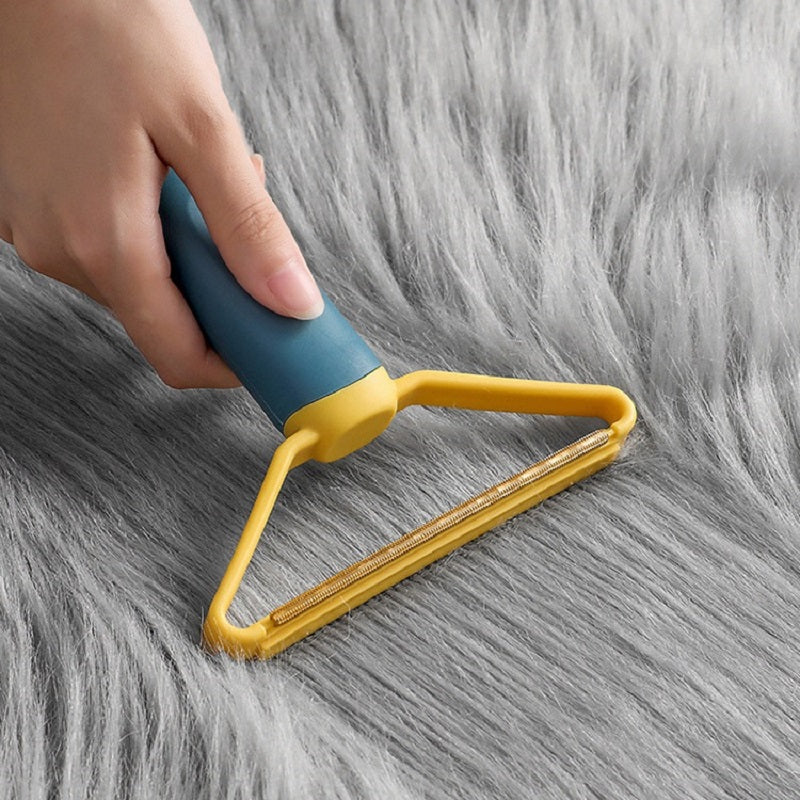Hand using blue and yellow pet hair remover on long-pile grey fabric — reusable dog and cat hair remover for furniture