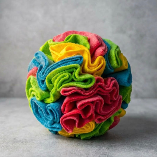 Dog snuffle ball in bright multicolour fleece — pink, blue, green and yellow — on grey concrete background — interactive dog nose work toy