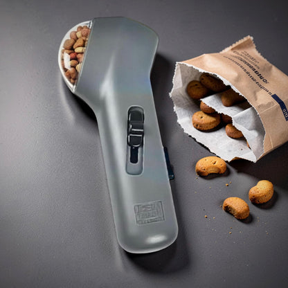 Grey pet treat launcher lying flat on a grey surface next to an open bag of dog biscuits — dog training treat dispenser