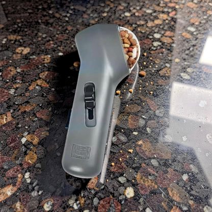 Grey pet treat launcher loaded with dog treats resting on shiny kitchen work top with crumbs around it — dog training treat shooter