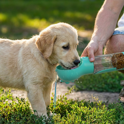 Golden retriever puppy drinking from teal multi-purpose dog bottle held by owner on grass — portable water and food bottle for dogs