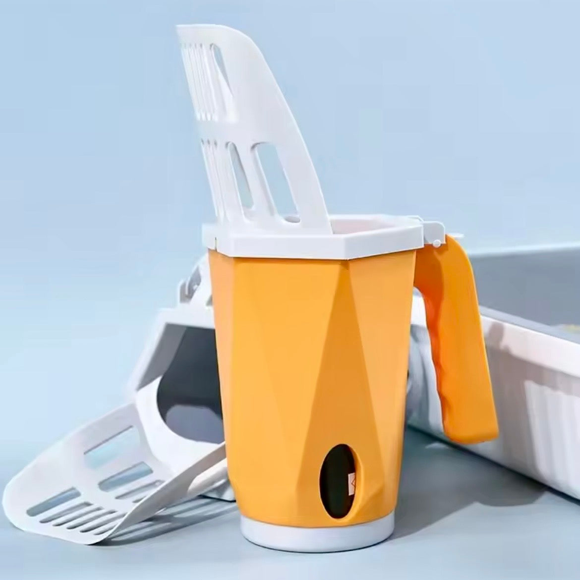 Orange cat litter scoop with integrated waste bag dispenser standing upright next to white cat litter box on blue background