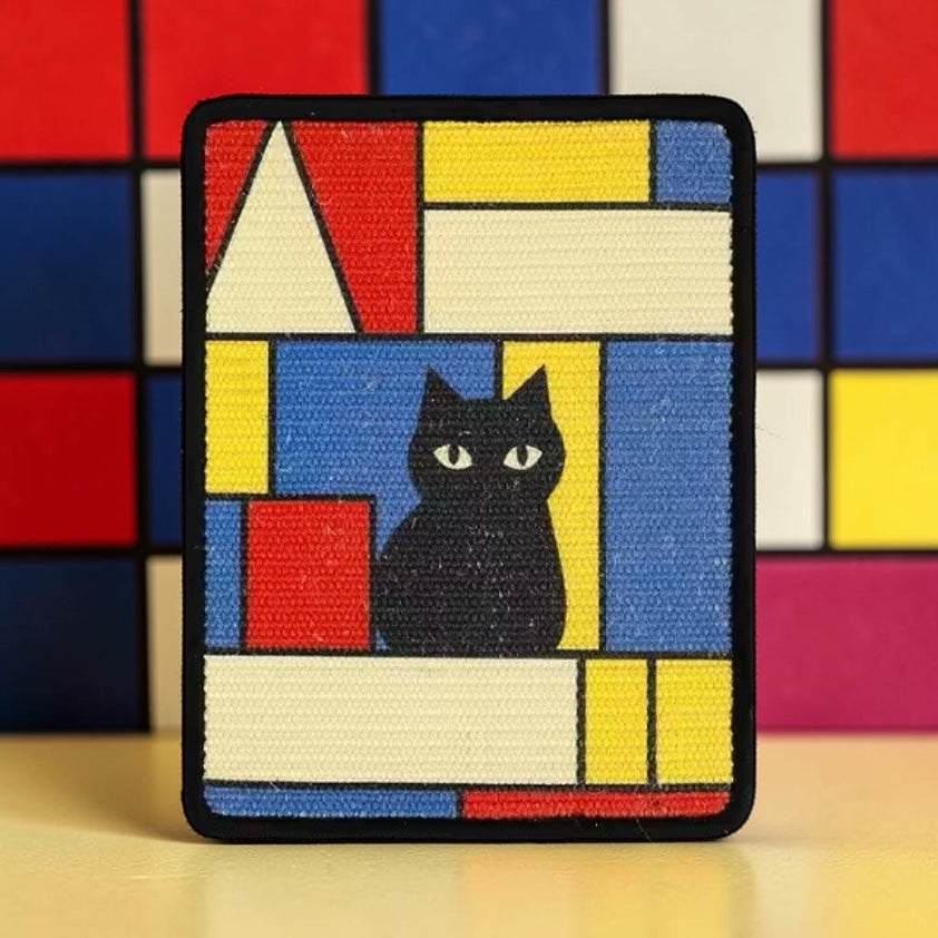 Wall-mounted sisal cat scratcher with Mondrian-style geometric design in red, yellow and blue with black cat — decorative cat scratching pad